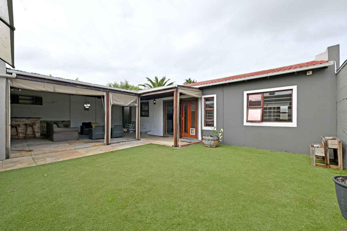Rear view of the property featuring a covered patio area with tiled flooring, timber pergola, and a well-maintained artificial lawn garden.