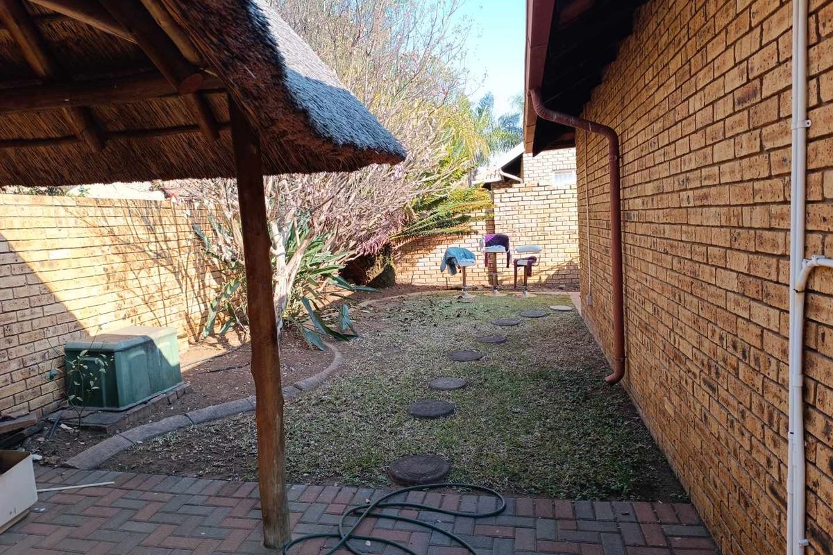 A rear garden area featuring a thatch roof lapa, brick paving, and facebrick exterior walls.