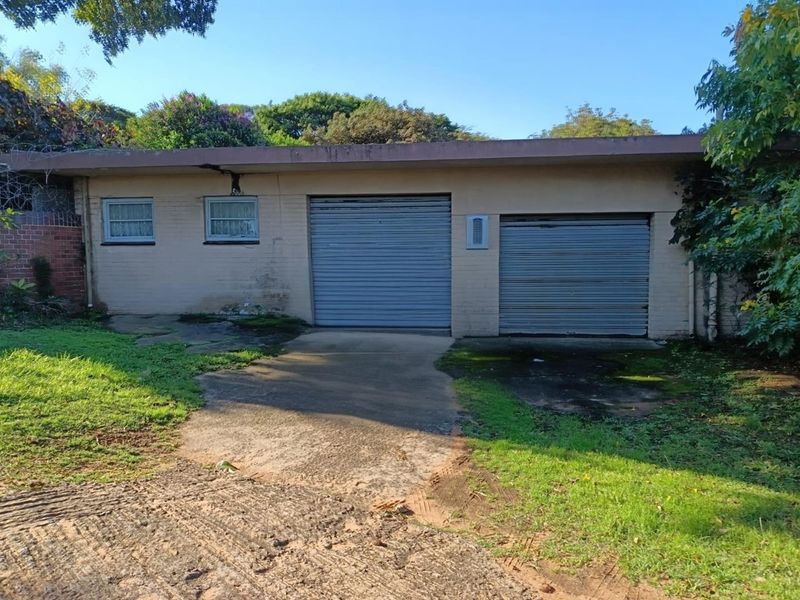 A detached double garage featuring roller doors and a concrete driveway, showing signs of significant weathering and exterior maintenance requirements.