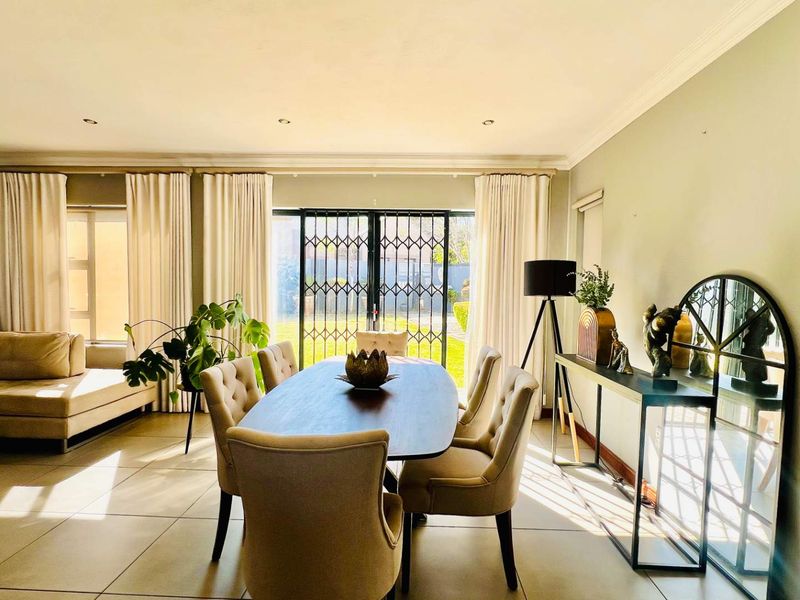 Spacious open-plan living and dining area featuring large sliding doors with security gates, tiled flooring, and recessed lighting, offering direct access to the garden.