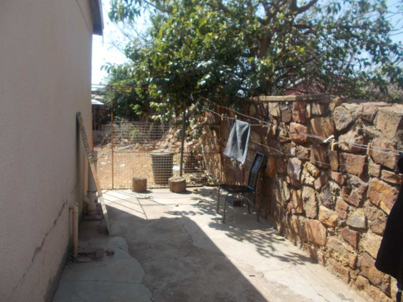 A rear exterior area featuring a stone boundary wall, concrete paving, and a wire mesh gate, showing signs of wear and cracking.