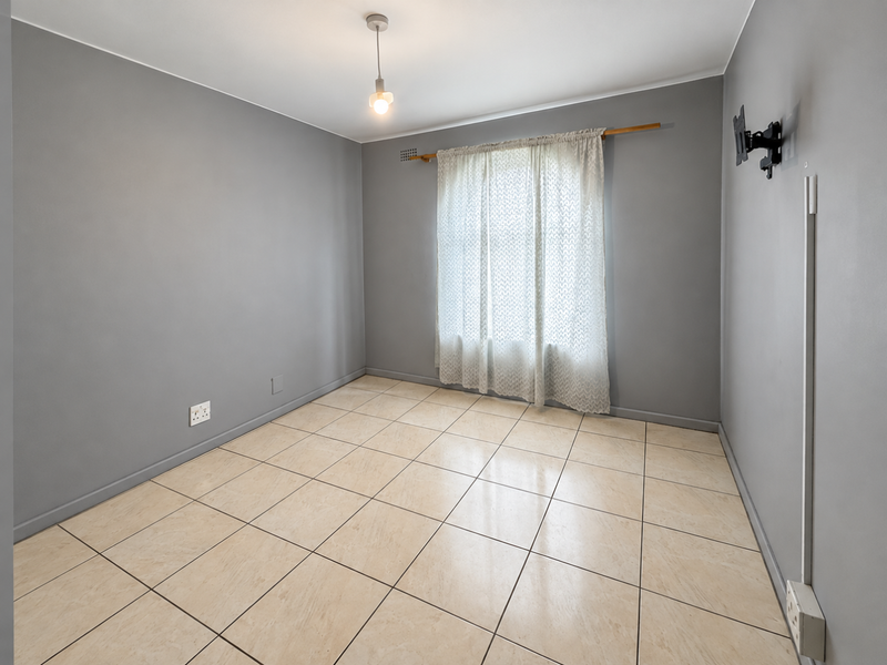 An empty bedroom featuring neutral grey walls, tiled flooring, and a simple pendant light fixture, ready for personalization.