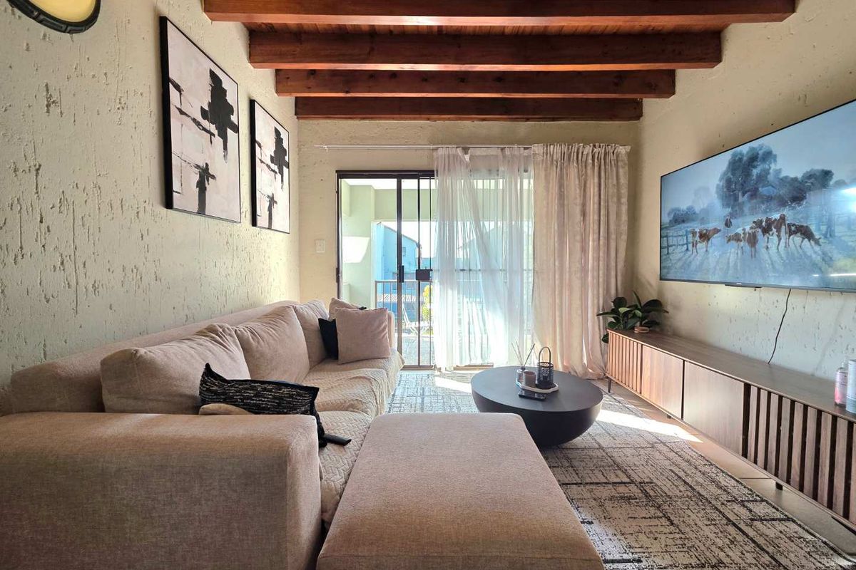 Cozy living room featuring exposed timber ceiling beams, textured plaster walls, and a sliding glass door providing access to the balcony.