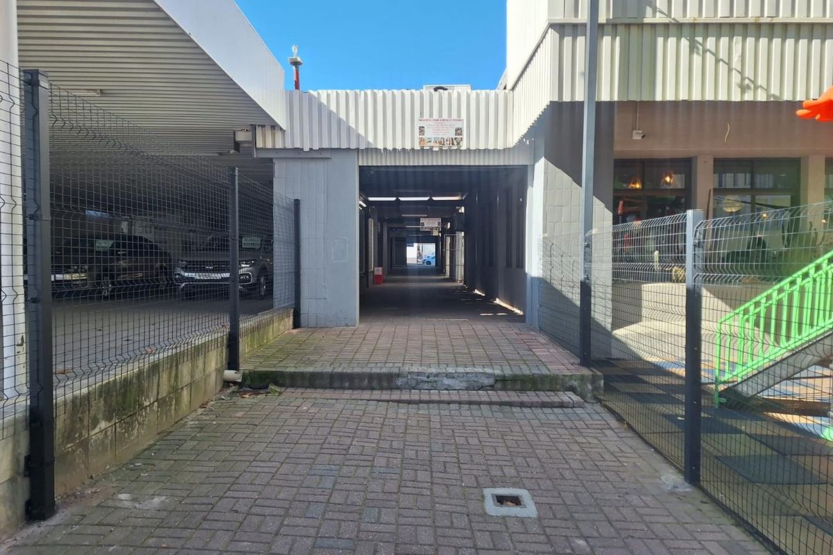 A paved exterior walkway leading between office building sections, featuring metal fencing and corrugated cladding with a covered passage.