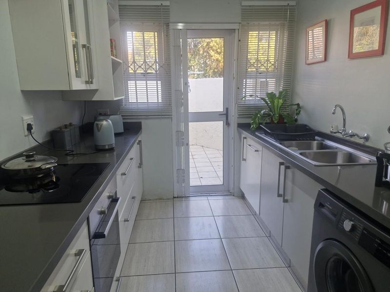 A functional galley-style kitchen featuring white cabinetry, stone countertops, integrated appliances, and direct access to an outdoor patio area.