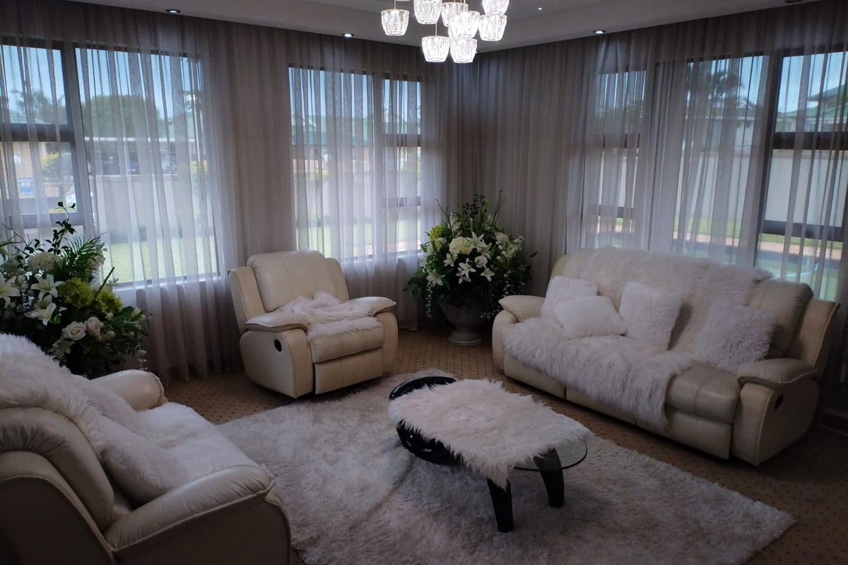A well-lit living room featuring large windows with floor-to-ceiling curtains, recessed downlighting, and a contemporary chandelier.