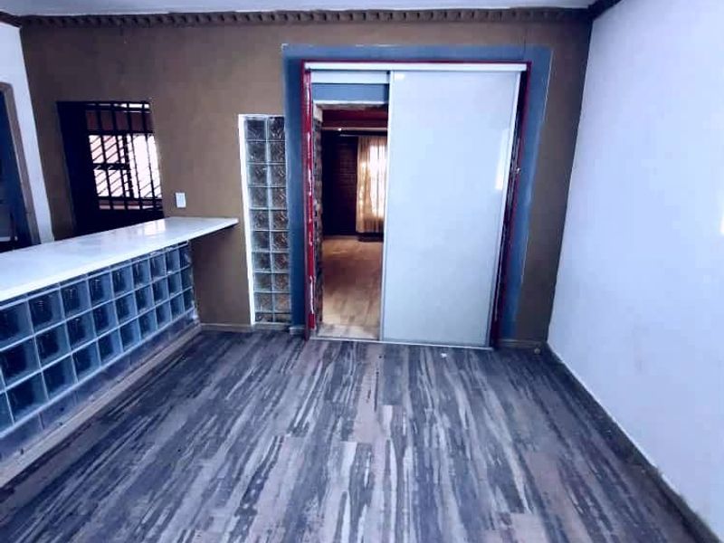 An empty living area featuring laminate flooring, a glass block partition, and a sliding door leading to an adjacent room.