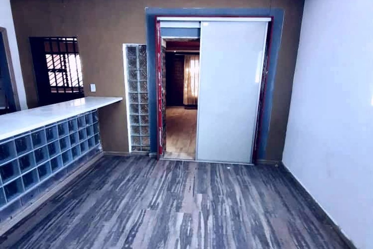 An empty living area featuring laminate flooring, a glass block partition, and a sliding door leading to an adjacent room.