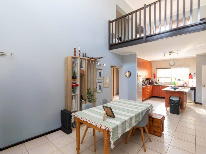 Open-plan living and kitchen area featuring double-height ceilings, tiled flooring, and a mezzanine level with a timber balustrade overlooking the main space.