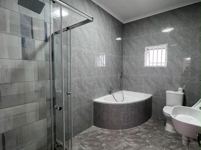 Modern bathroom featuring a glass-enclosed shower, a built-in corner bathtub, a pedestal basin, and contemporary grey marble-look wall and floor tiling.