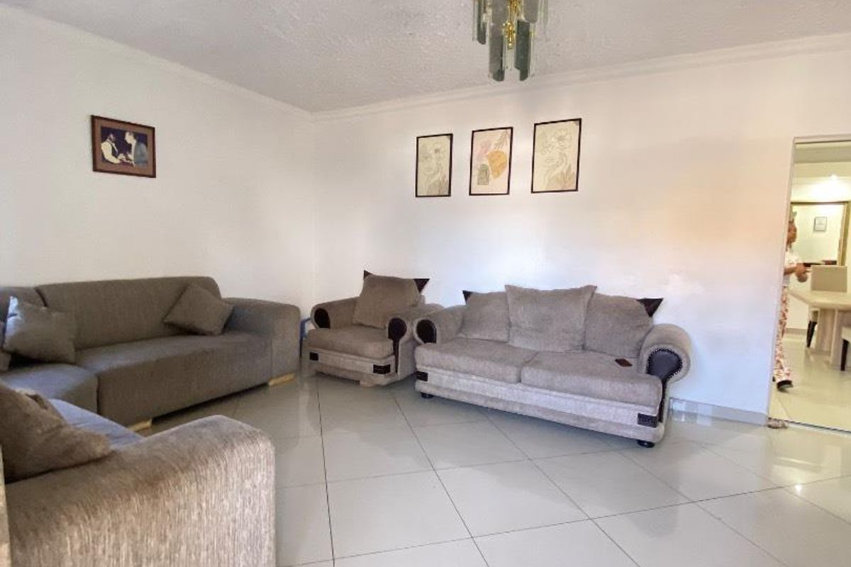 Spacious living room featuring large format floor tiles, a decorative chandelier, and neutral wall finishes.