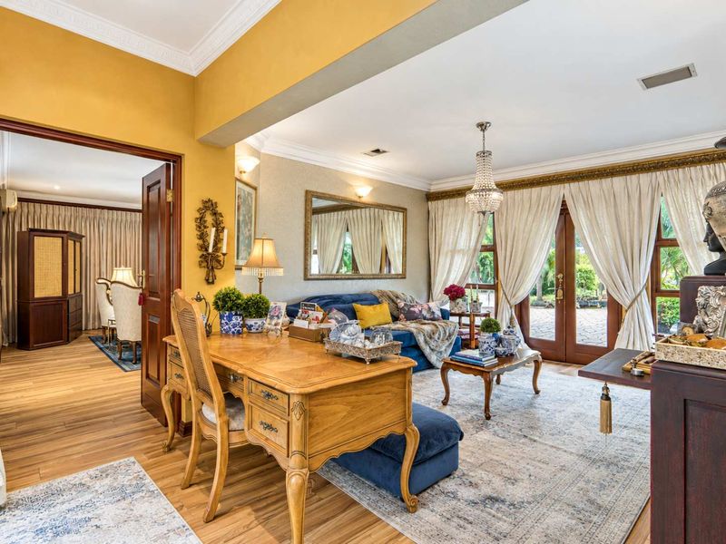 A well-maintained living room featuring hardwood flooring, crown molding, a crystal chandelier, and French doors providing access to the outdoor area.