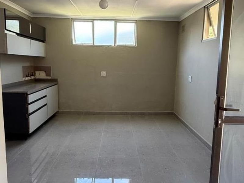 An empty kitchen area featuring tiled flooring, built-in cabinetry with countertops, and natural light from casement windows.