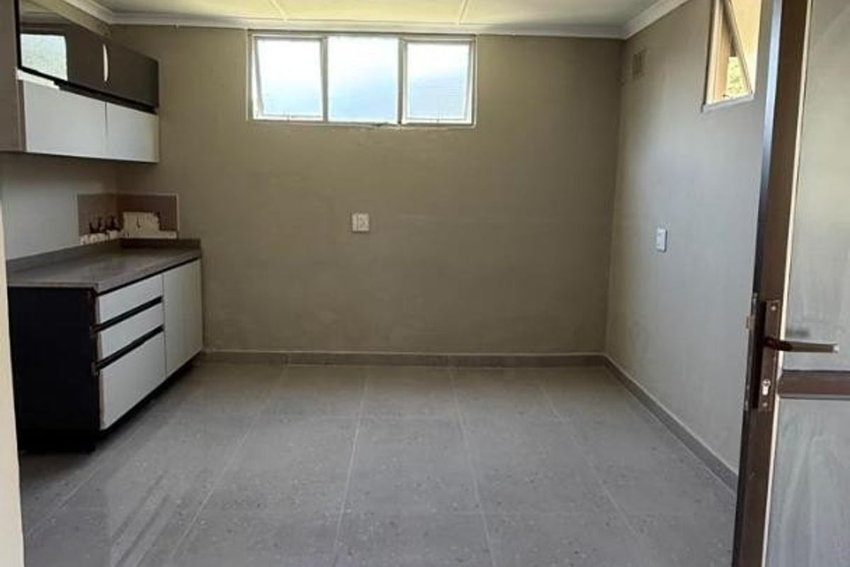 An empty kitchen area featuring tiled flooring, built-in cabinetry with countertops, and natural light from casement windows.