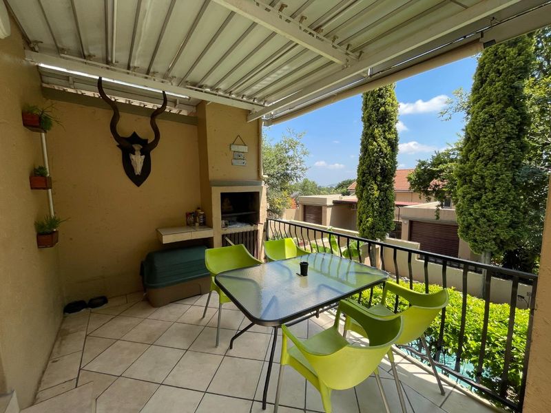 Covered balcony featuring a built-in braai, tiled flooring, and metal railings, offering an outdoor entertainment space with views of the surrounding complex.