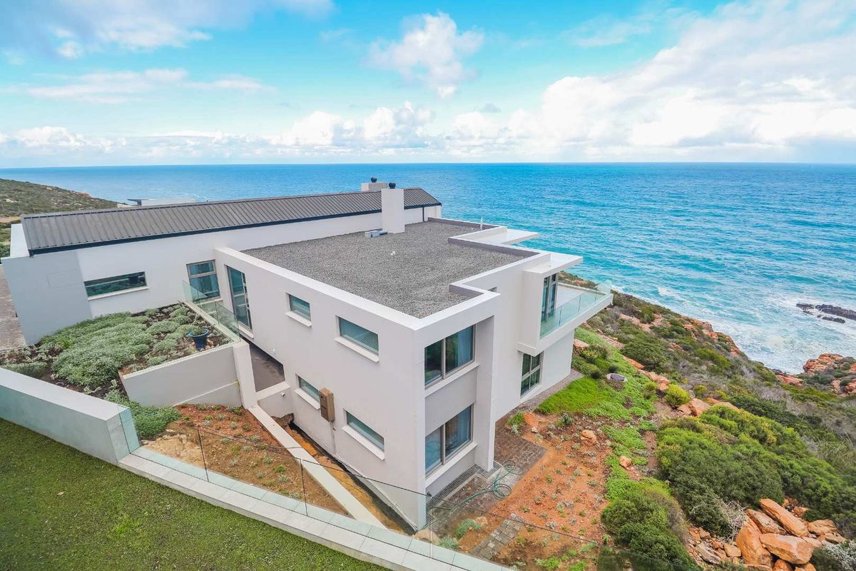 Aerial view of a modern coastal residence featuring a flat roof, glass balustrades, and expansive ocean views.