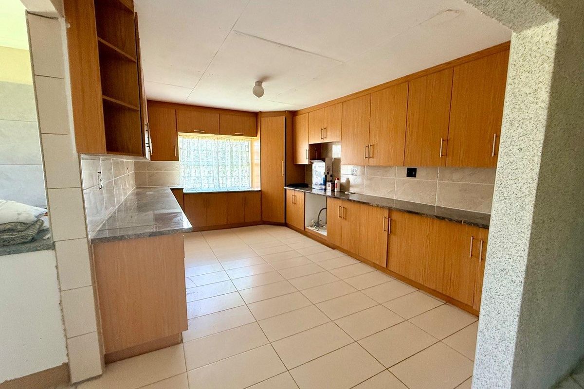 A functional kitchen featuring wood-look cabinetry, tiled flooring, and ample countertop workspace, offering a practical layout for daily meal preparation.