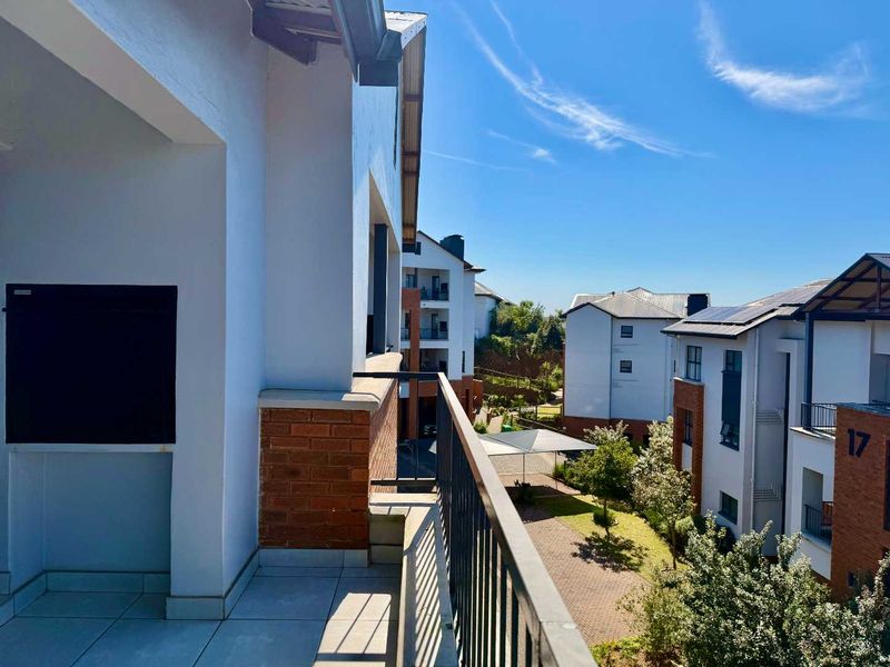 A spacious balcony featuring a built-in braai, metal balustrade, and tiled flooring, offering views over the apartment complex grounds.