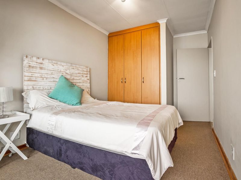A functional bedroom featuring neutral wall tones, carpeted flooring, and a built-in wooden wardrobe providing ample storage space.