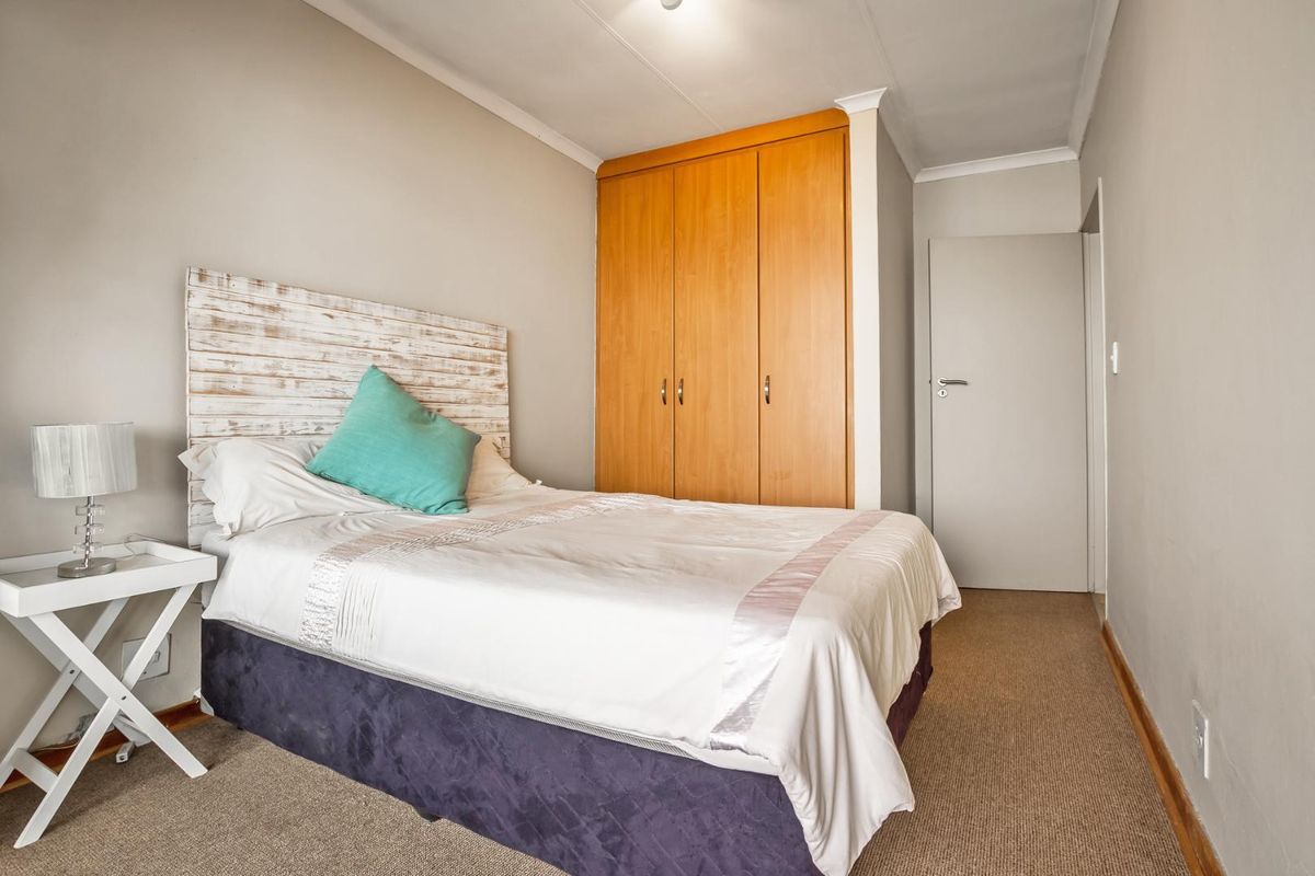 A functional bedroom featuring neutral wall tones, carpeted flooring, and a built-in wooden wardrobe providing ample storage space.