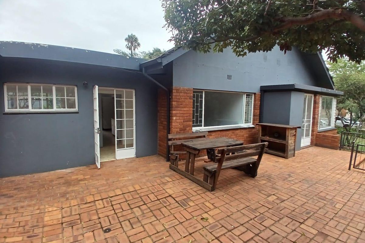 Rear exterior view of the apartment featuring a brick paved patio area, painted brick walls, and classic steel-framed windows and doors.
