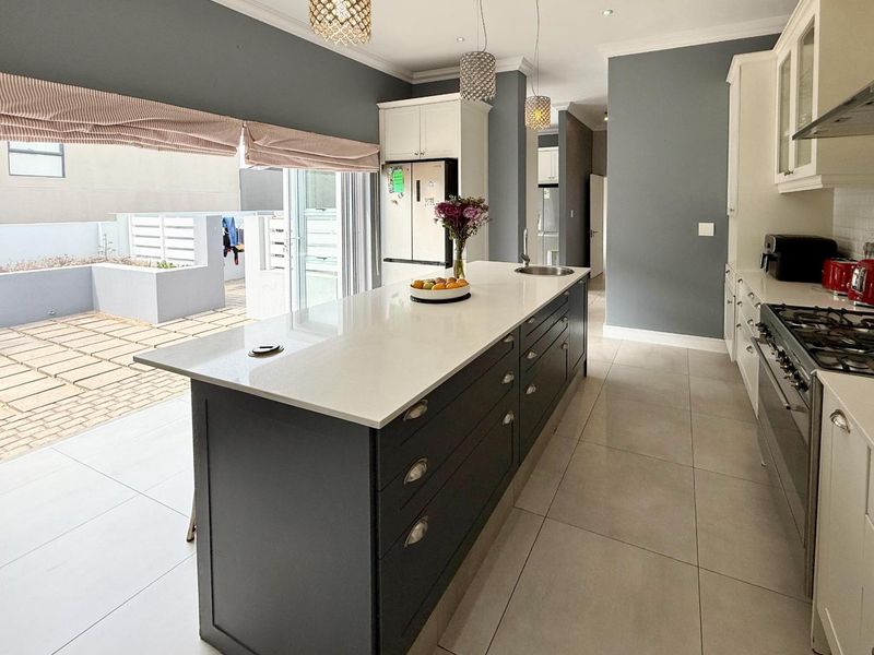 Modern kitchen featuring a large central island with quartz countertops, gas stove, ample cabinetry, and seamless flow to an outdoor patio area.