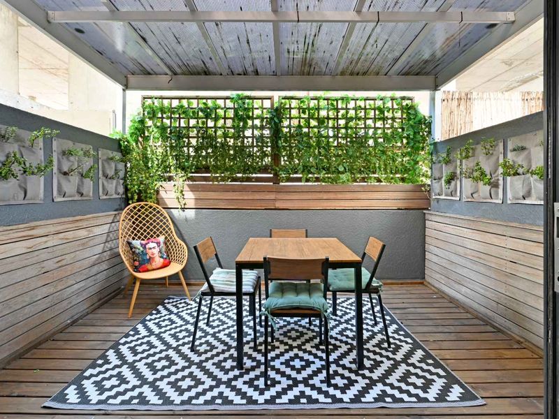 A well-maintained covered balcony featuring timber decking, wood-paneled walls, and a polycarbonate roof, creating a private outdoor dining space.