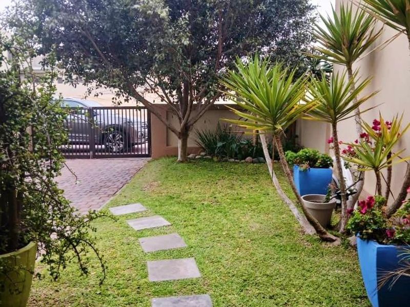 A well-maintained garden area featuring a stone pathway, lush lawn, mature tree, and secure gated driveway access.