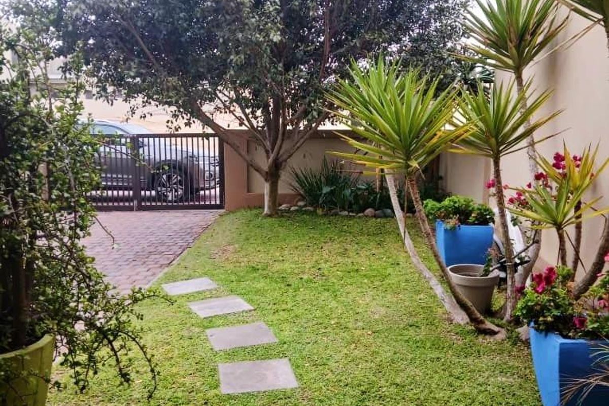 A well-maintained garden area featuring a stone pathway, lush lawn, mature tree, and secure gated driveway access.