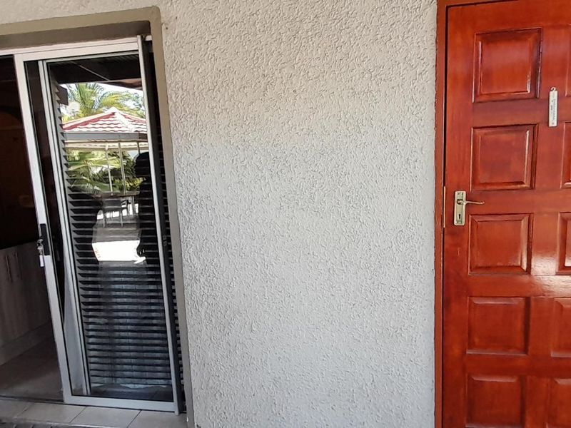 Exterior view of an apartment entrance featuring a solid timber panel door and a sliding glass door providing access to the interior.