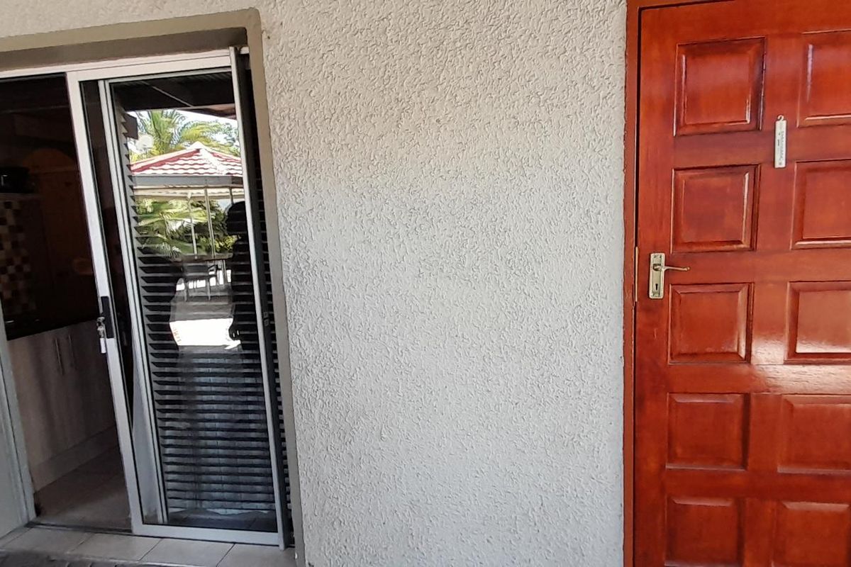 Exterior view of an apartment entrance featuring a solid timber panel door and a sliding glass door providing access to the interior.