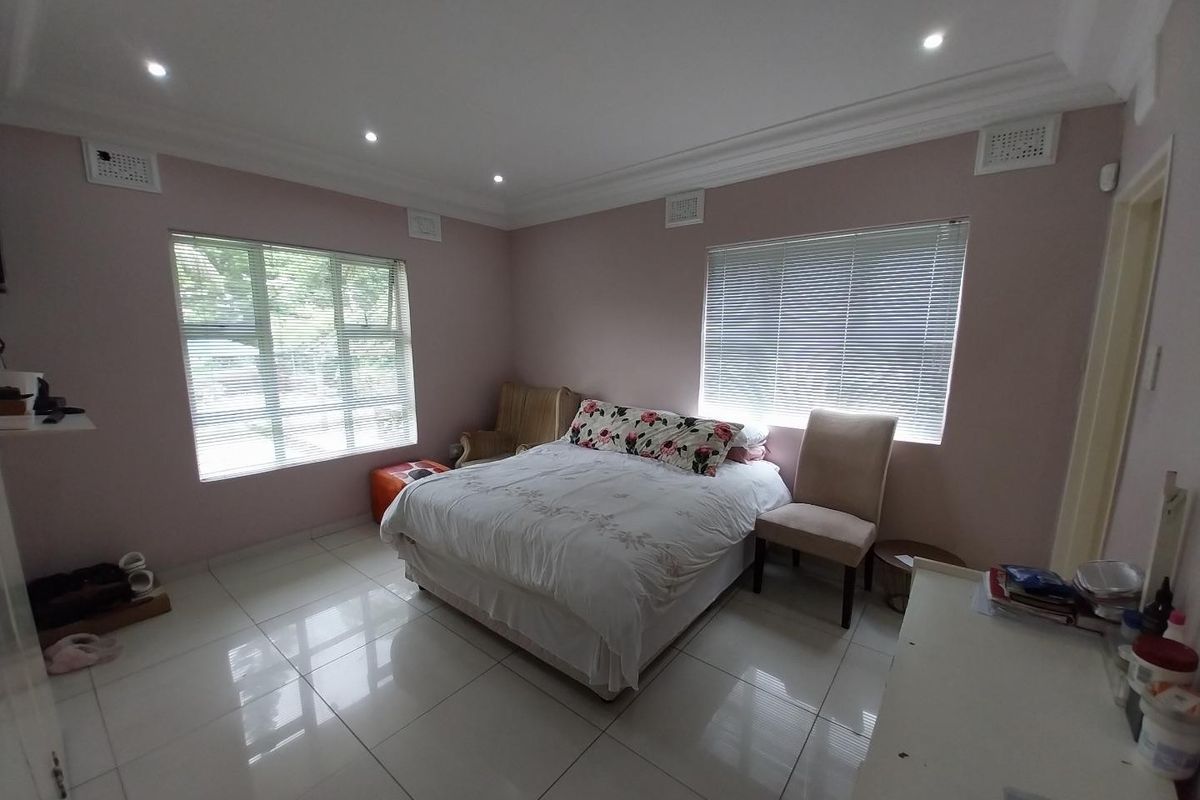 A well-lit bedroom featuring tiled flooring, recessed downlighting, decorative cornice, and dual windows with fitted venetian blinds.