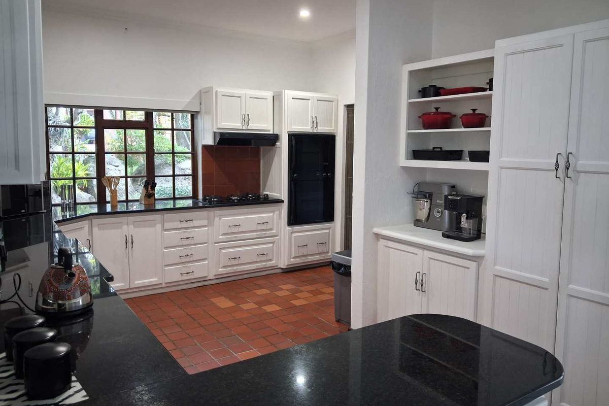 A well-maintained kitchen featuring white cabinetry, dark granite countertops, a gas hob, built-in oven, and terracotta floor tiles with a garden view.