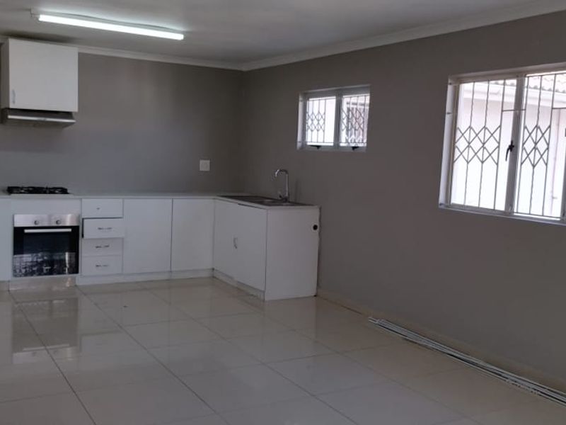 Spacious open-plan kitchen and living area featuring modern white cabinetry, built-in oven, gas hob, and large neutral floor tiles.