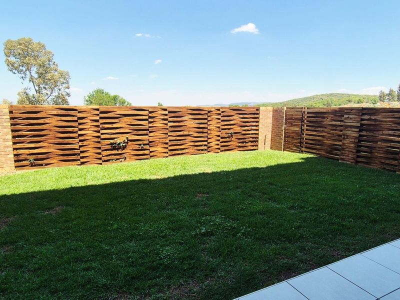 A private garden area featuring a well-maintained lawn, enclosed by decorative timber slat fencing and brick boundary walls, adjacent to a tiled patio.