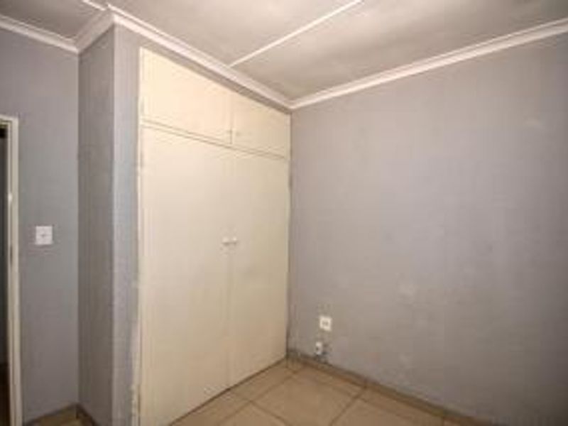 An empty bedroom featuring tiled flooring, a built-in wardrobe, and coved ceiling details, ready for personalization.