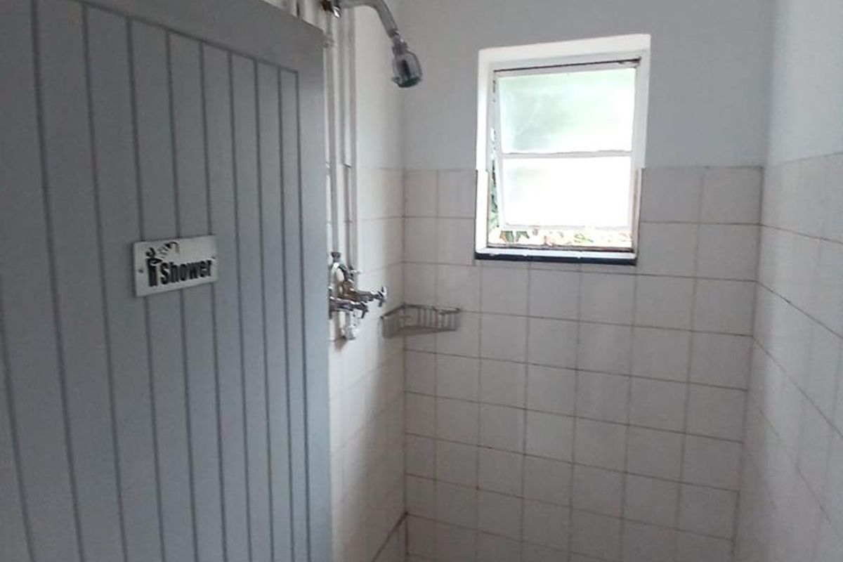 A compact shower area featuring tiled walls, a small window for ventilation, and exposed plumbing fixtures.