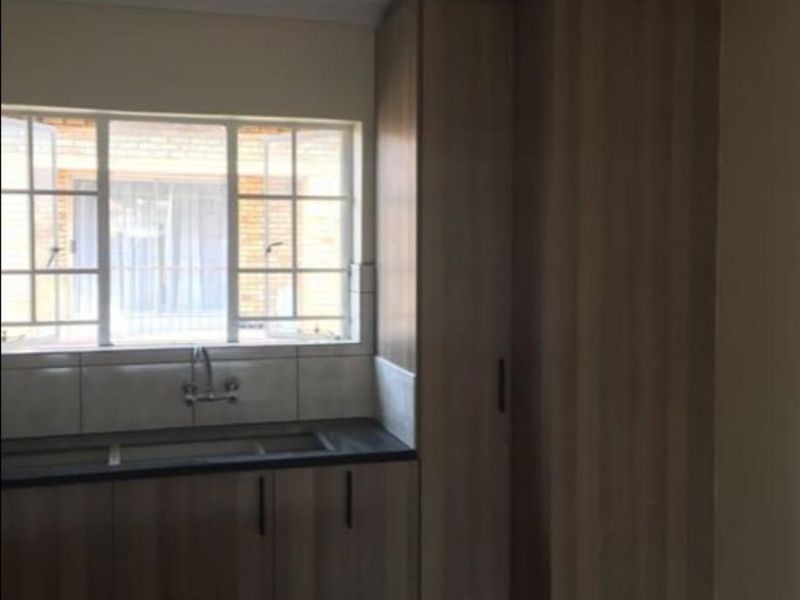 A functional kitchen area featuring wood-look built-in cabinetry, dark laminate countertops, a double sink, and a tiled splashback under a window.