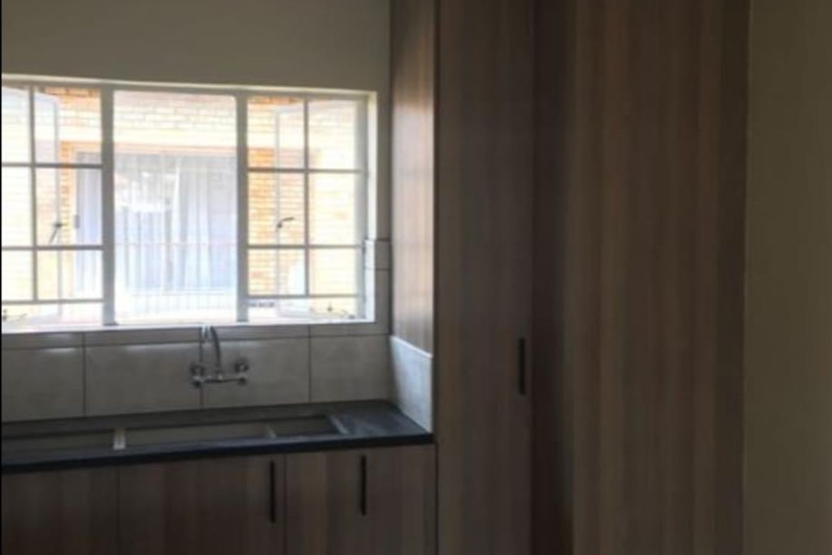 A functional kitchen area featuring wood-look built-in cabinetry, dark laminate countertops, a double sink, and a tiled splashback under a window.