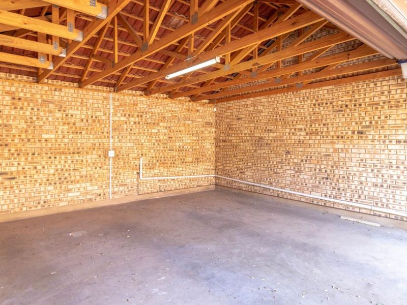A spacious, empty garage featuring exposed timber roof trusses, facebrick walls, and a concrete floor, providing ample storage or parking space.