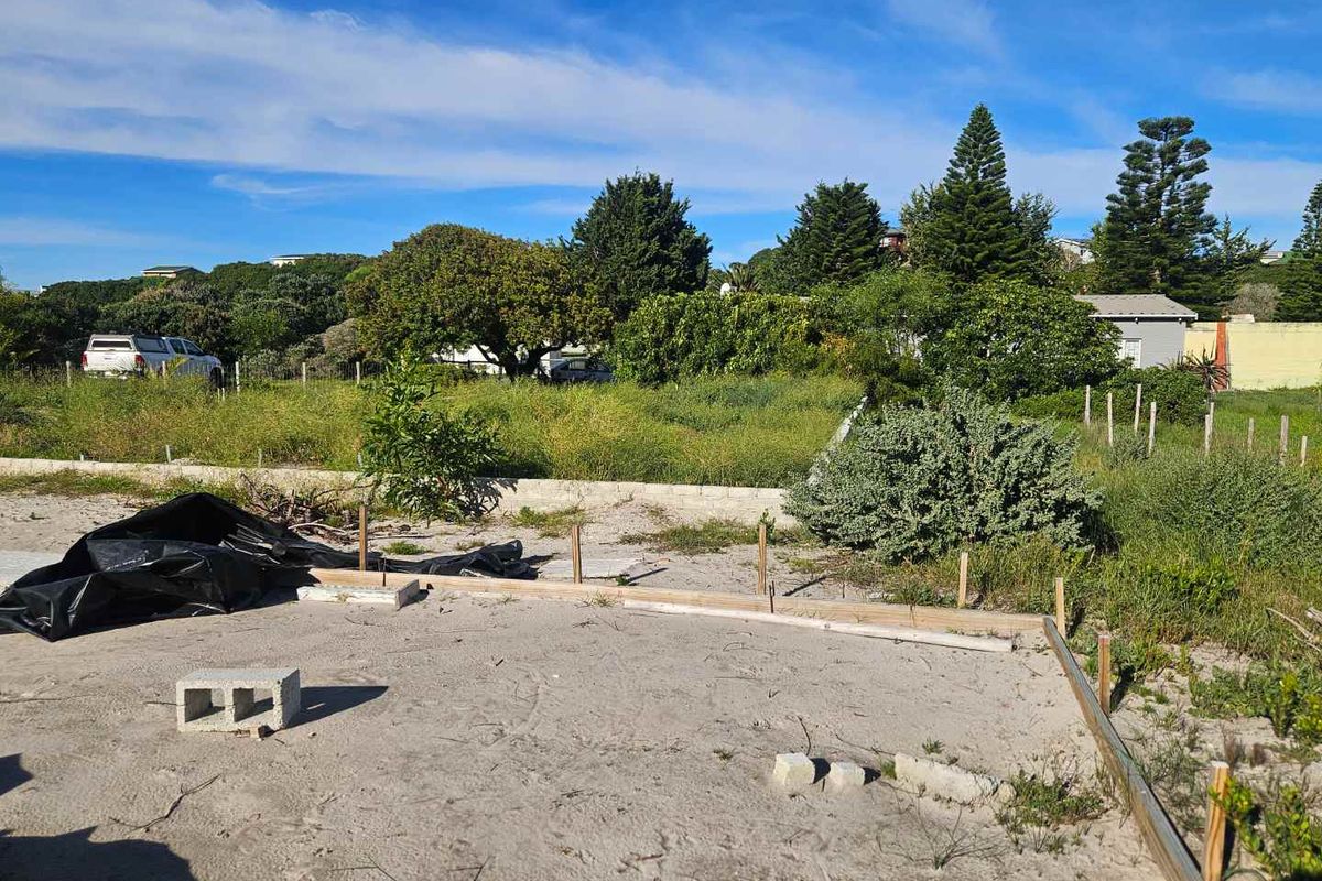 A vacant residential plot featuring initial foundation formwork and a boundary wall, set within a established neighborhood.