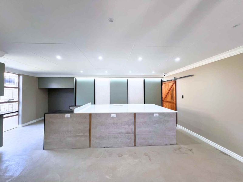 Modern kitchen space featuring a large central island with stone countertops, recessed lighting, and a rustic sliding barn door, presented in a clean, empty state.