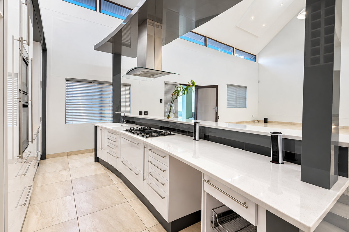 Modern, high-ceilinged kitchen featuring sleek cabinetry, stone countertops, integrated appliances, and large windows that provide ample natural light.