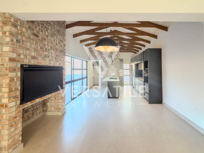 Spacious open-plan living and kitchen area featuring exposed timber beams, a brick fireplace, and modern cabinetry in a well-maintained townhouse setting.