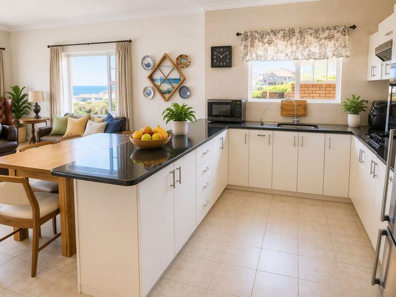 An open-plan kitchen and living area featuring white cabinetry, granite countertops, ceramic tile flooring, and views of the surrounding landscape.