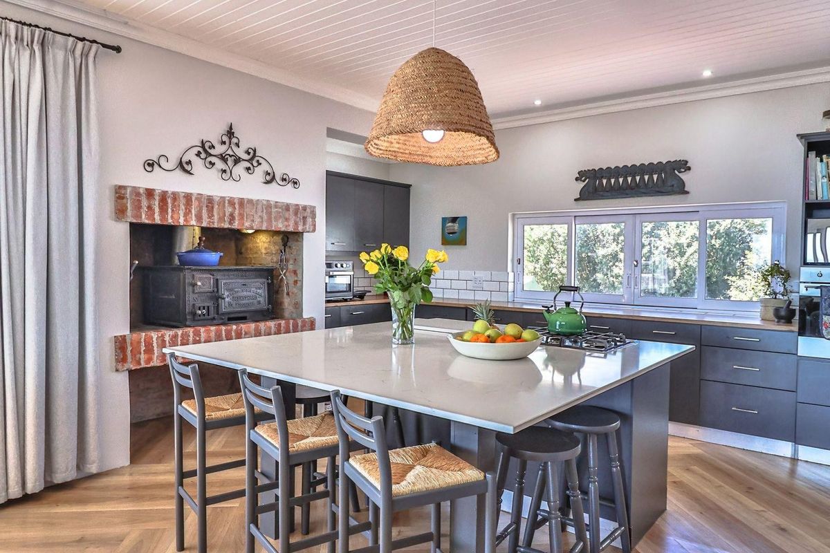 Modern kitchen featuring a large central island with stone countertop, built-in oven, gas hob, and a unique brick-surround fireplace feature.