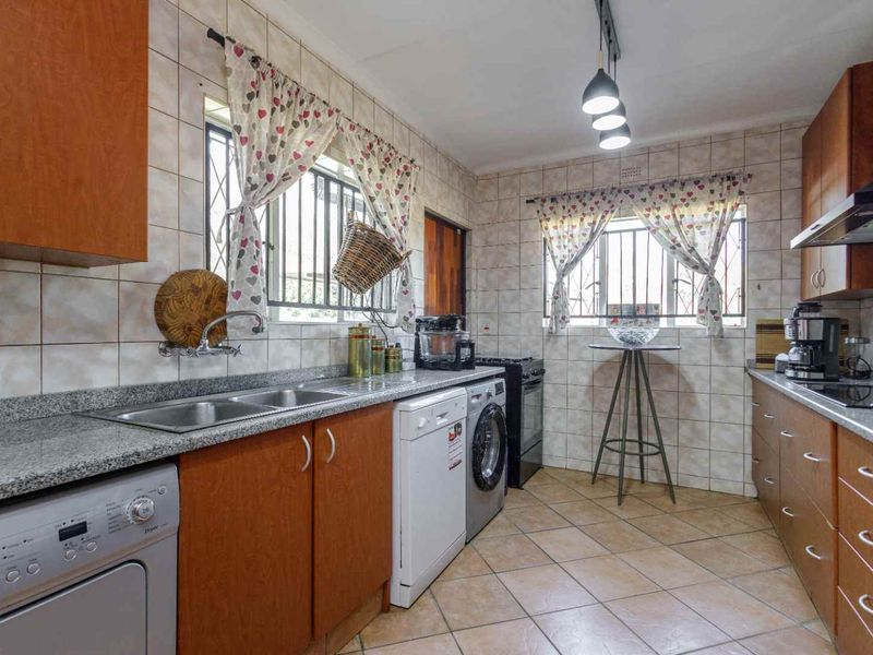 A functional kitchen featuring granite countertops, double sink, tiled backsplash, and ample built-in cabinetry with integrated appliance spaces.