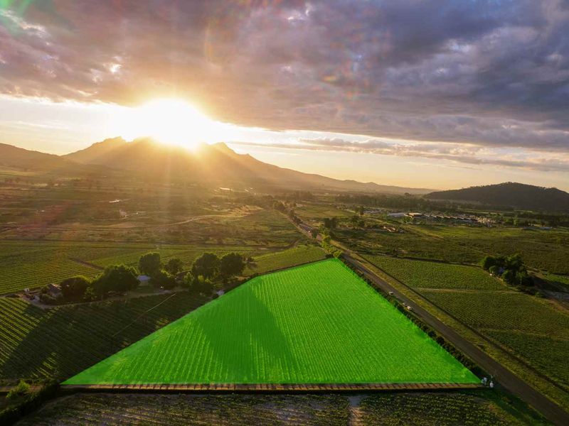 An aerial view of a large, open agricultural plot highlighted in green, set against a scenic mountain landscape at sunset.
