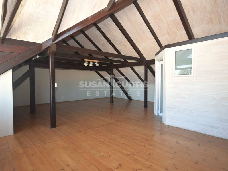 Spacious open-plan living area featuring a high vaulted ceiling with exposed timber beams and warm timber flooring throughout.