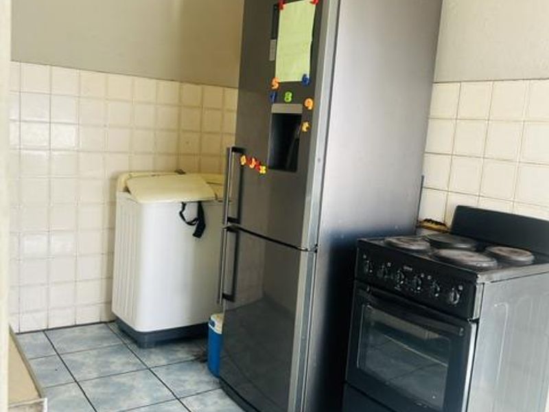 A functional kitchen area featuring tiled flooring, a tiled splashback, and a freestanding oven, requiring cosmetic updates to improve the overall finish.